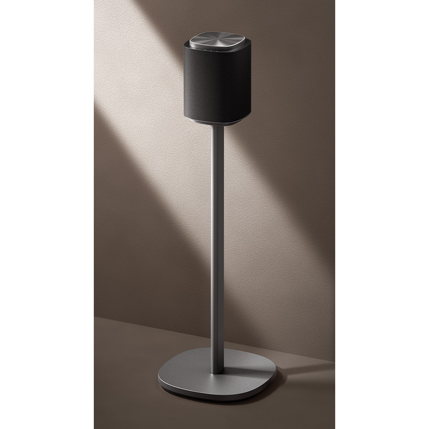 Black speaker on a gray stand against a muted wall with shadows.