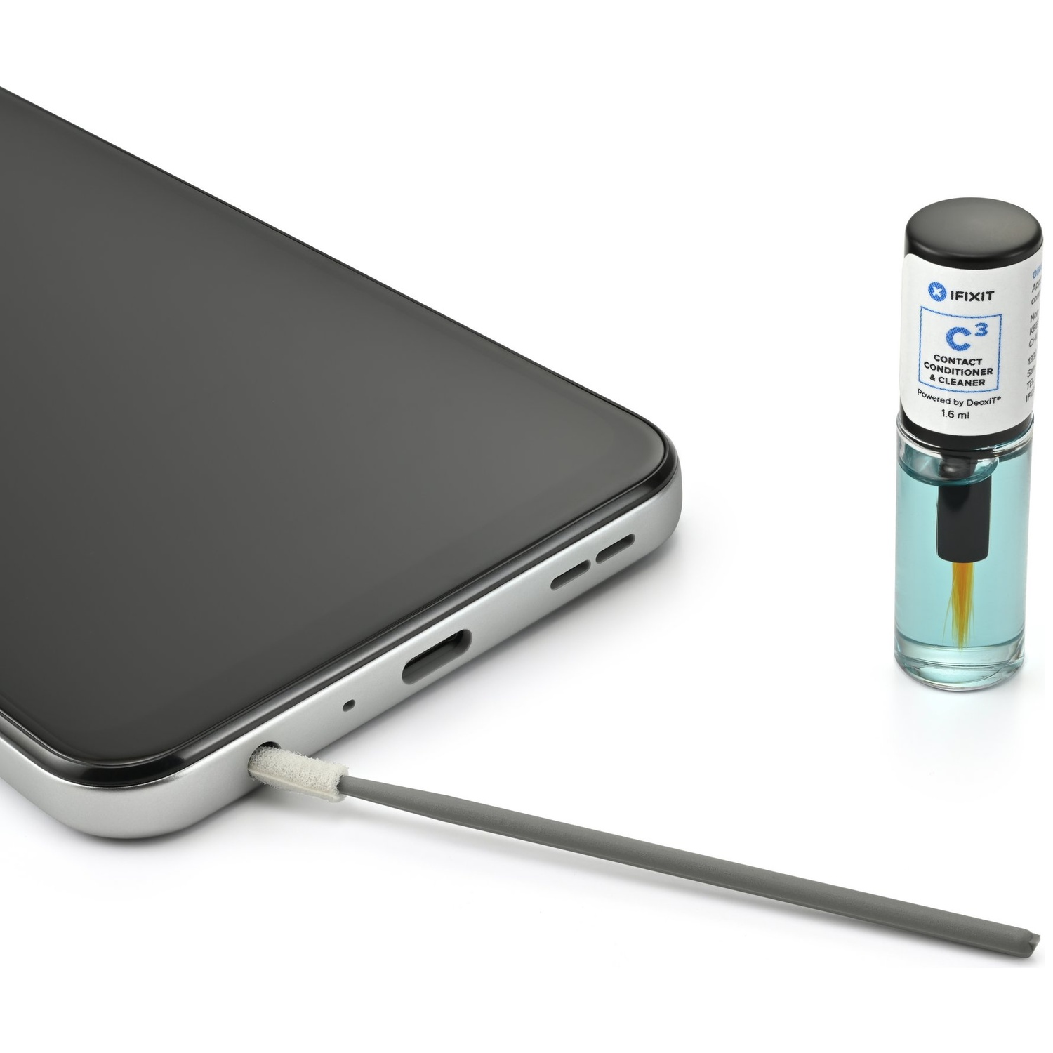 A gray cleaning swab is inserted into the charging port of a smartphone. A small bottle of contact cleaner is nearby.
