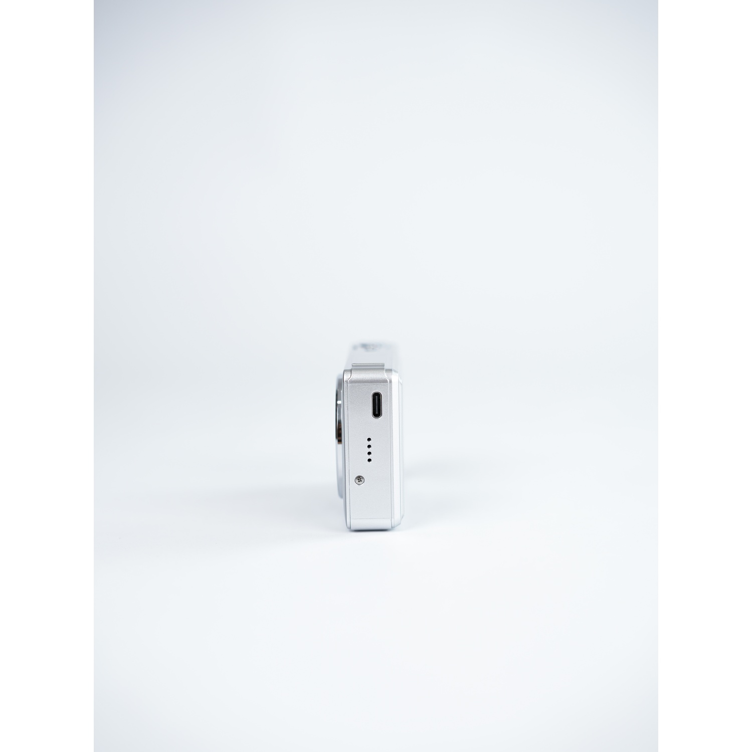 Fotocamera argento con porta USB-C e quattro spie su sfondo bianco.