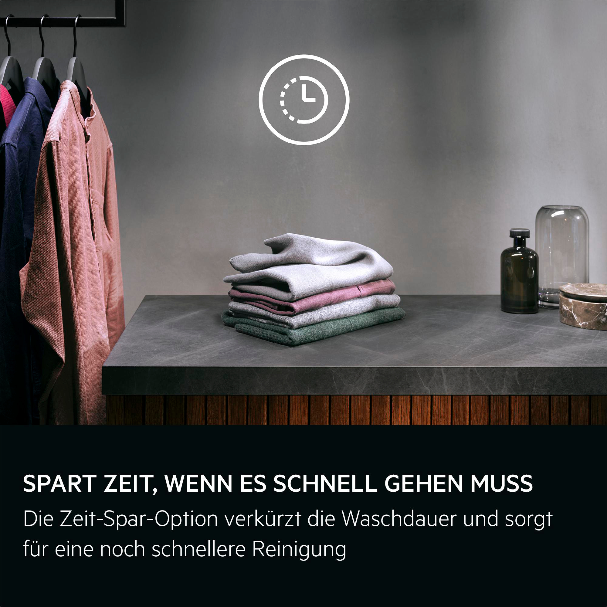 Kleidung auf Bügeln, gestapelte Kleidung und Deko-Objekte auf Tisch.