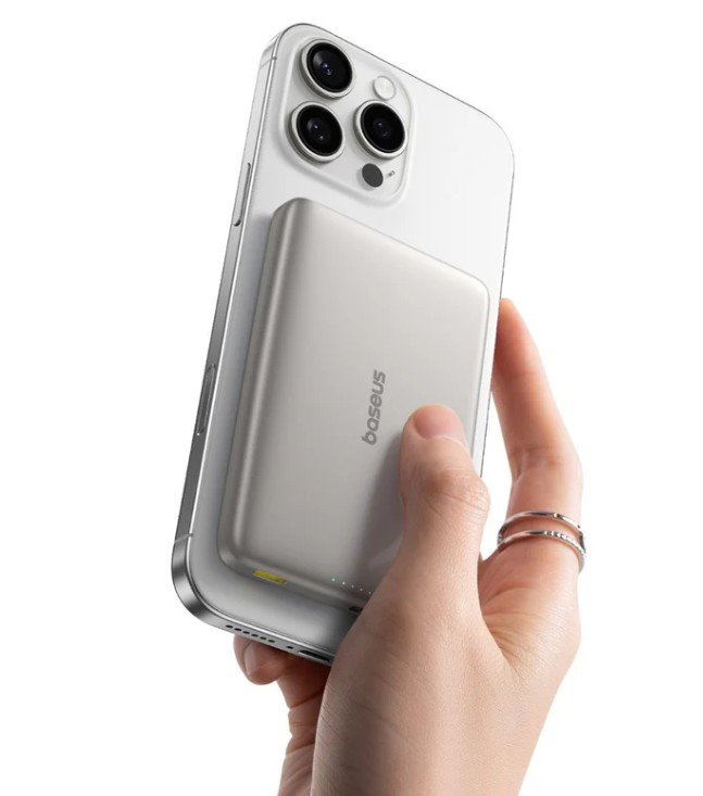 Gümüş iPhone'un arkasına takılı beyaz manyetik şarj cihazını bir el tutuyor.