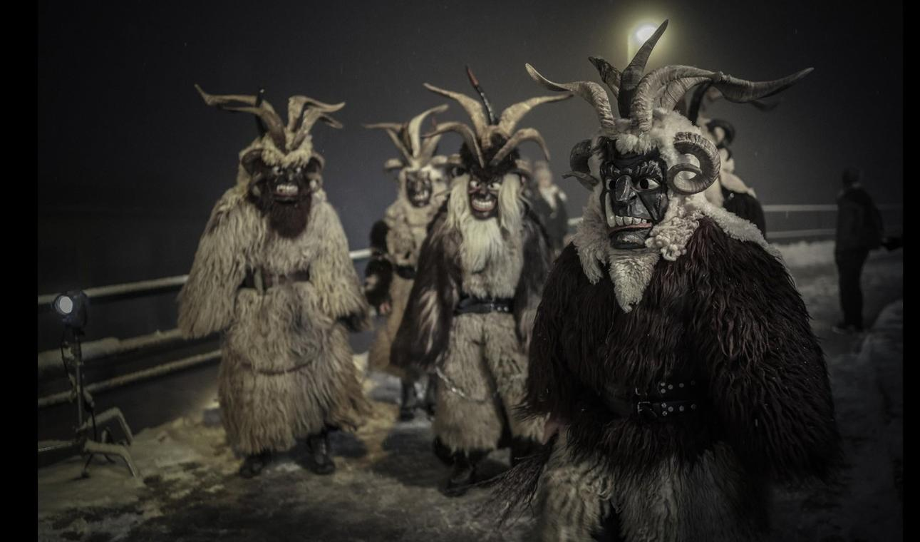 Mehrere gruselig maskierte Figuren in Pelzkostümen und mit Hörnern stehen im Schnee.