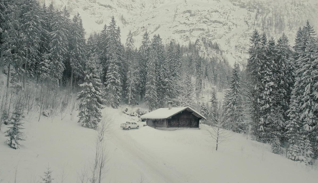 Ein Holzhaus mit einem Auto davor in einer verschneiten Berglandschaft.