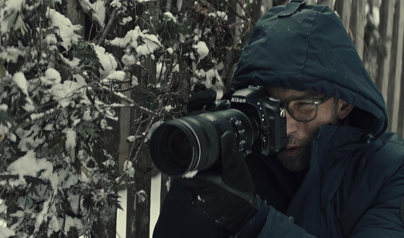 Ein Mann mit Brille fotografiert bei Schneefall durch eine Kamera.