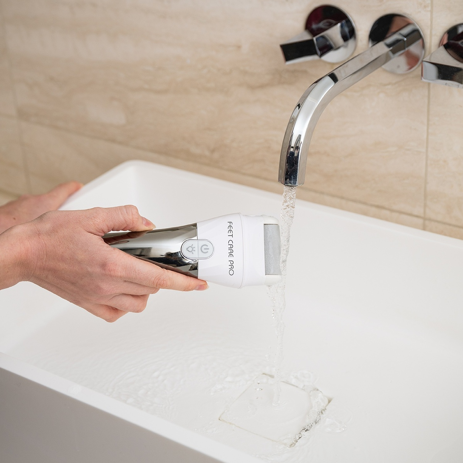 Una mano tiene un dispositivo bianco per la cura dei piedi sotto acqua corrente in un lavandino.