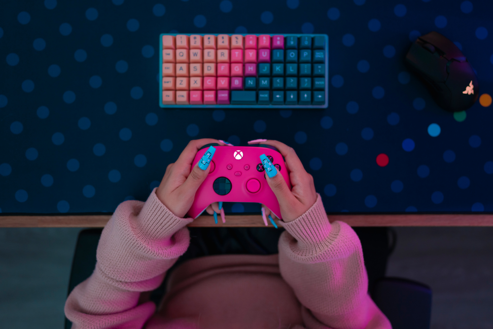 Persona sostiene mando rosa de Xbox, teclado y ratón sobre lunares azules.