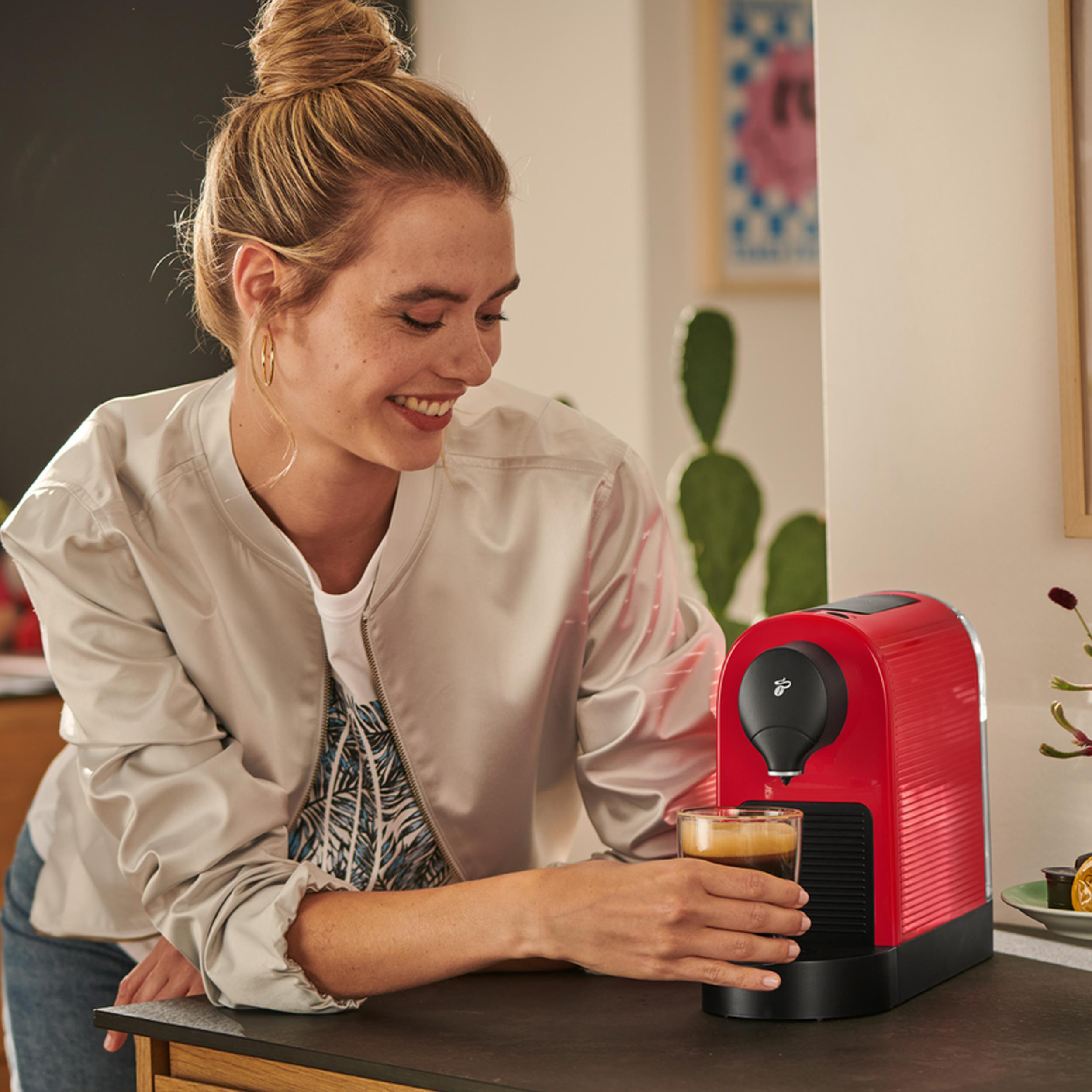 Eine Frau mit Dutt holt einen Espresso aus einer roten Kapselmaschine.