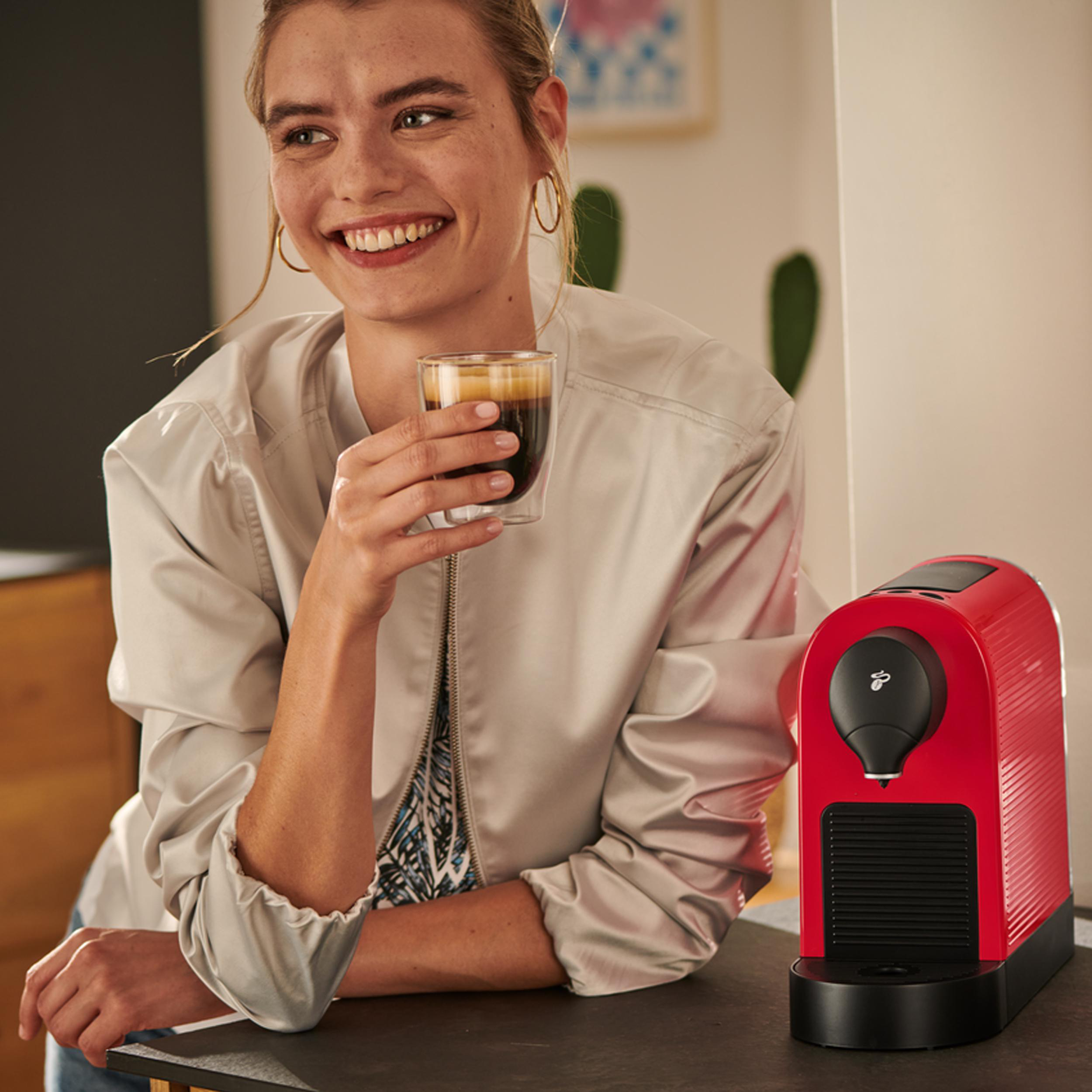 Eine Frau trinkt Kaffee neben einer roten Kaffeemaschine.