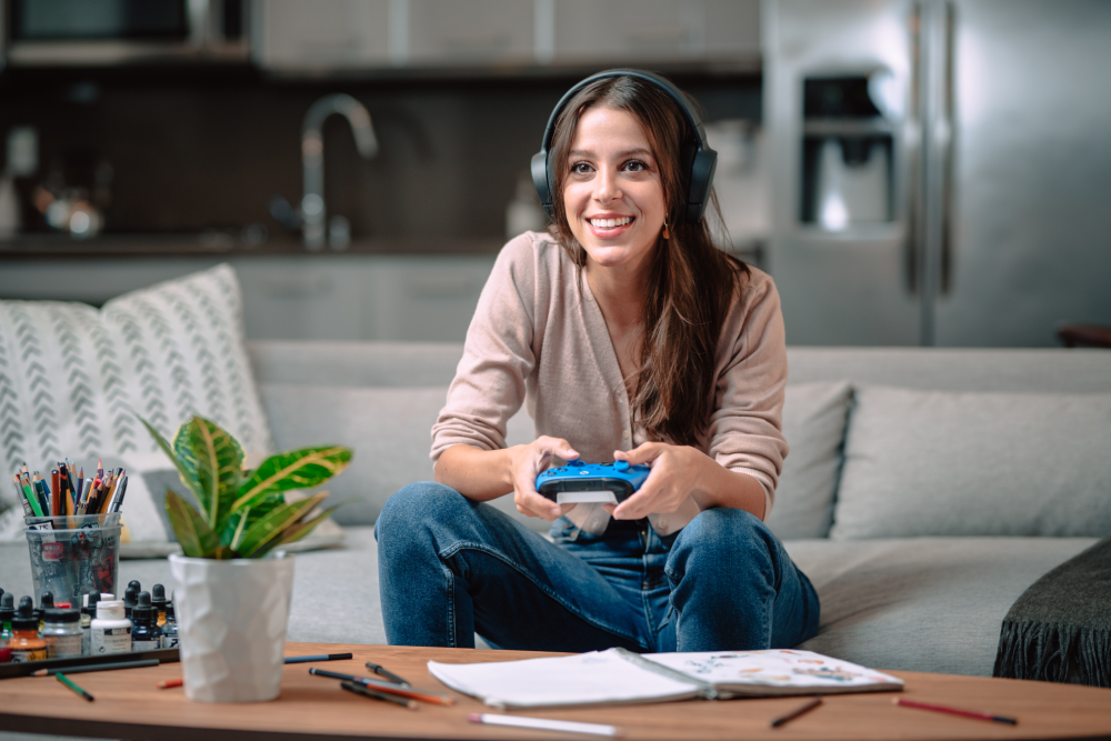 Mujer con auriculares juega videojuego con mando azul en el sofá.