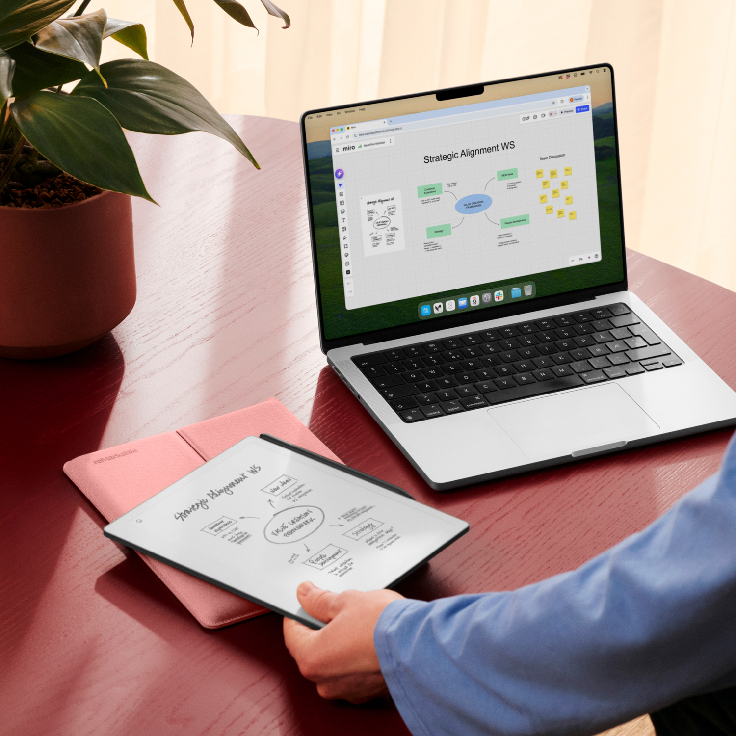 A laptop and tablet displaying diagrams and notes sit on a red desk.