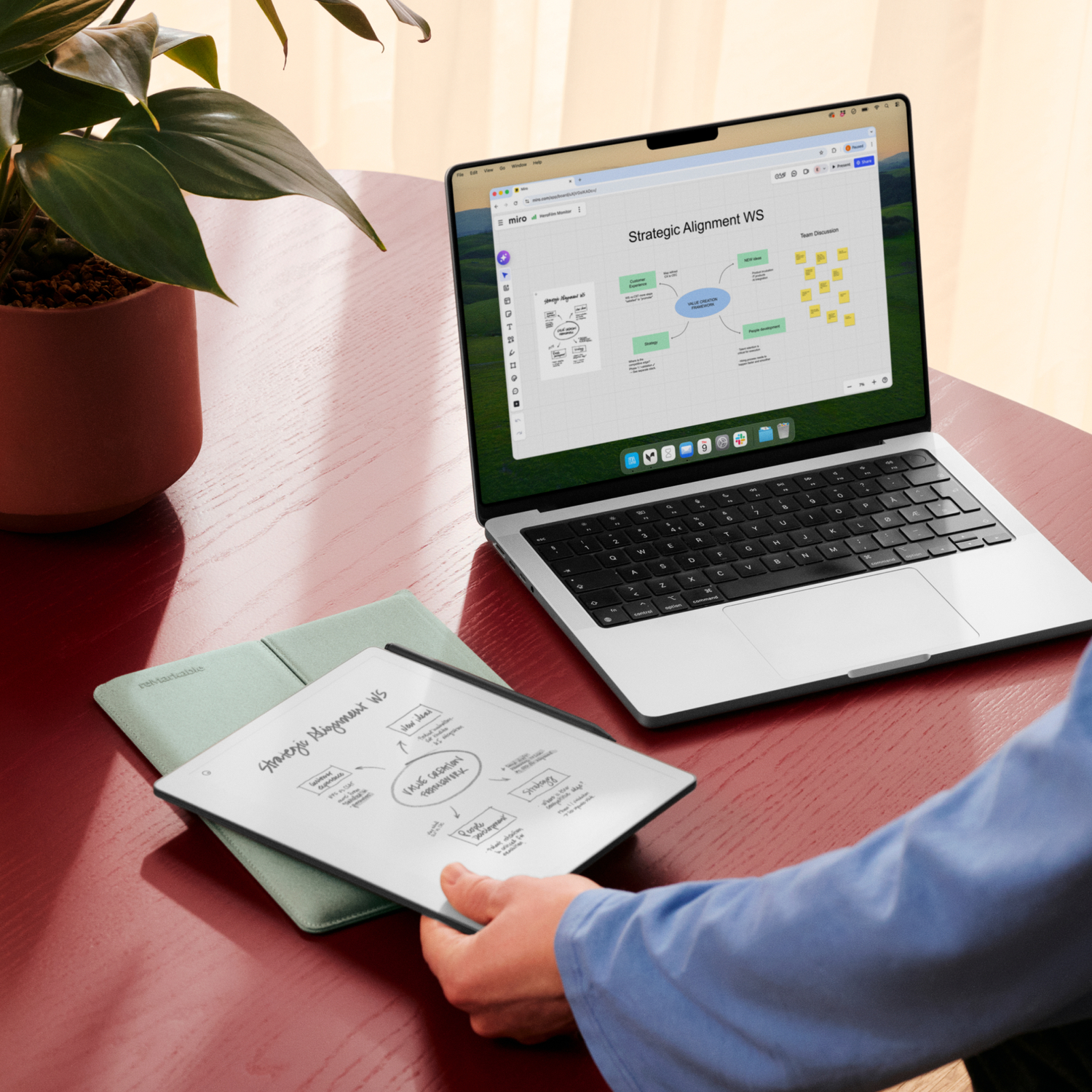 Laptop and tablet with diagrams on a red table, next to a plant.