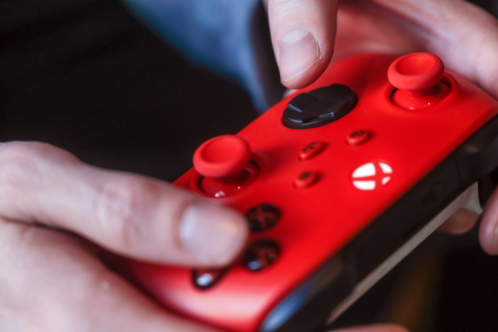 Manos sujetando un mando rojo con botones y joysticks negros.