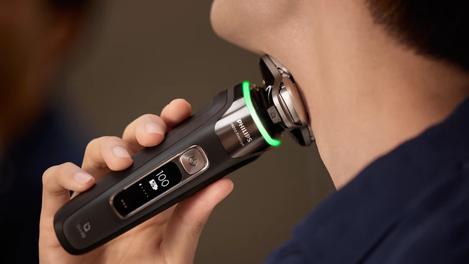 Mann rasiert sich mit einem schwarzen Philips Rasierer mit grüner Ladeanzeige.