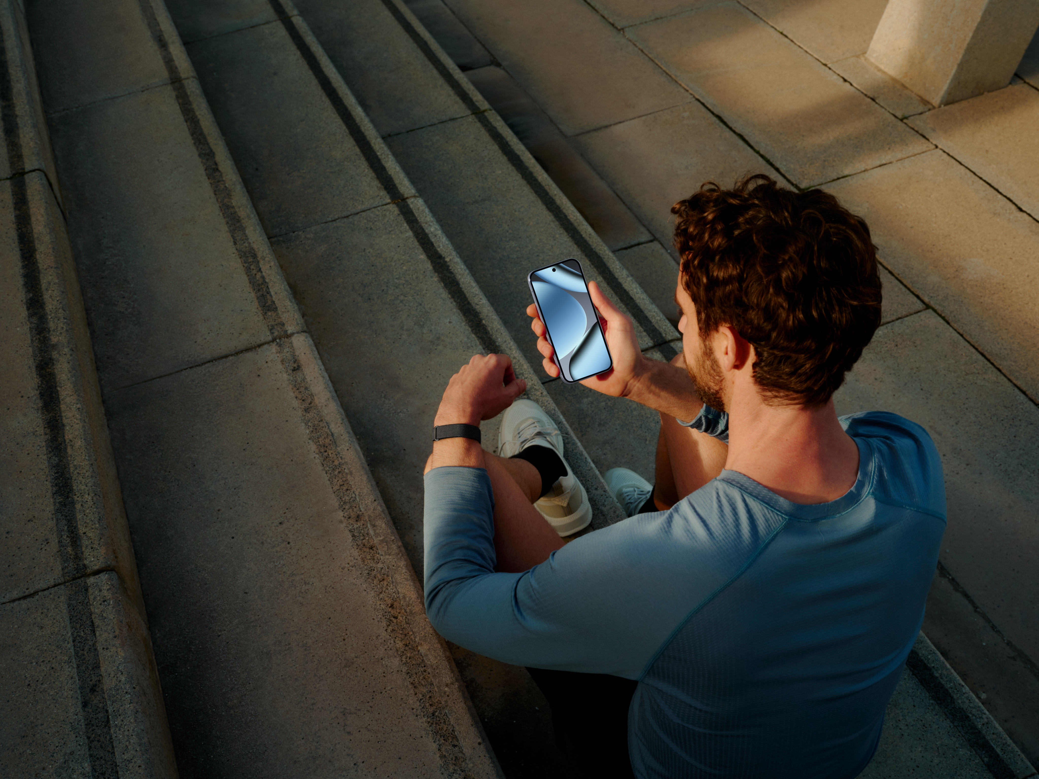 Mann sitzt auf Steinstufen und schaut auf sein Smartphone.