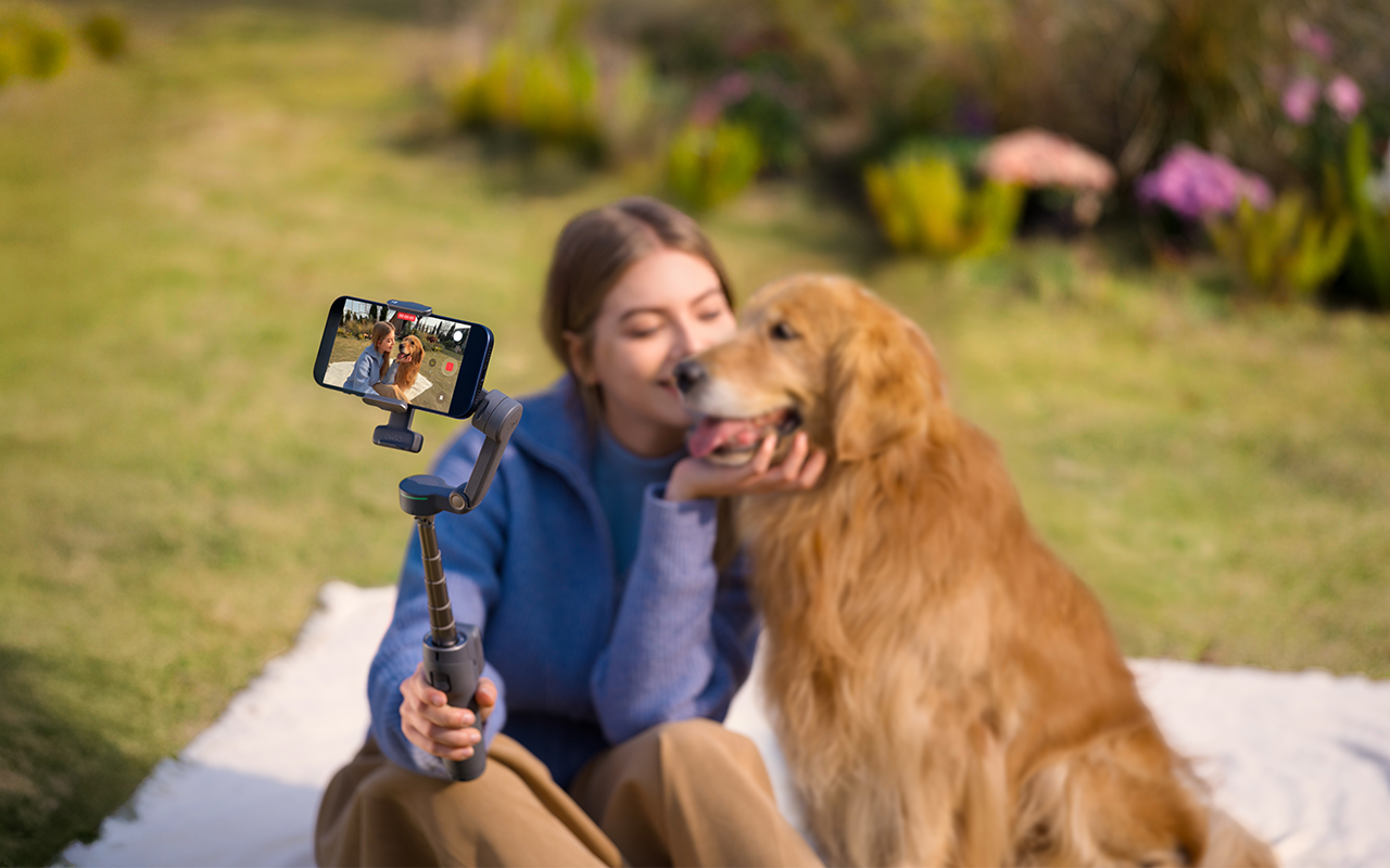 Frau filmt sich mit Golden Retriever in einem Gimbal im Freien.