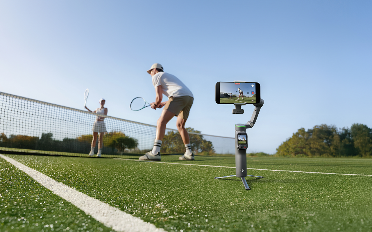 Gimbal mit Handy filmt Tennisspiel auf Platz. Zwei Spieler am Netz.