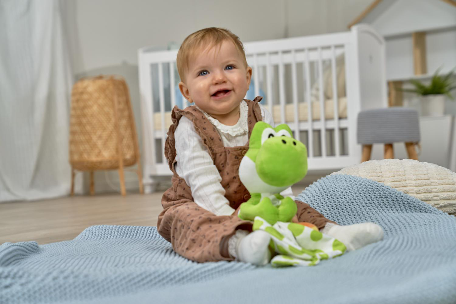 Ein Baby sitzt auf einer blauen Decke mit einem Yoshi-Plüschtier.