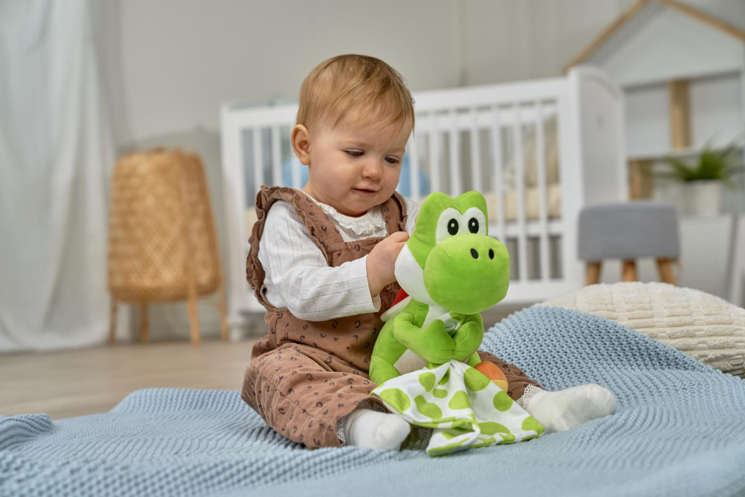 Ein Baby sitzt auf einer blauen Decke und spielt mit einer grünen Yoshi-Puppe.