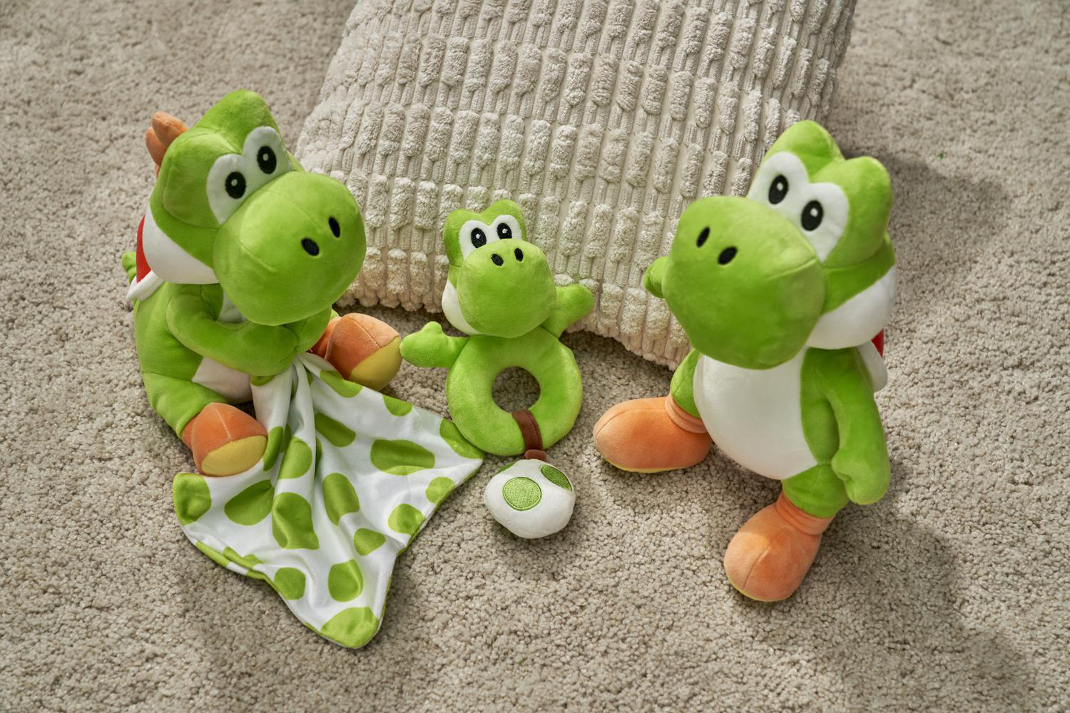 Drei grüne Yoshi-Plüschtiere und eine Decke liegen auf einem Teppich.