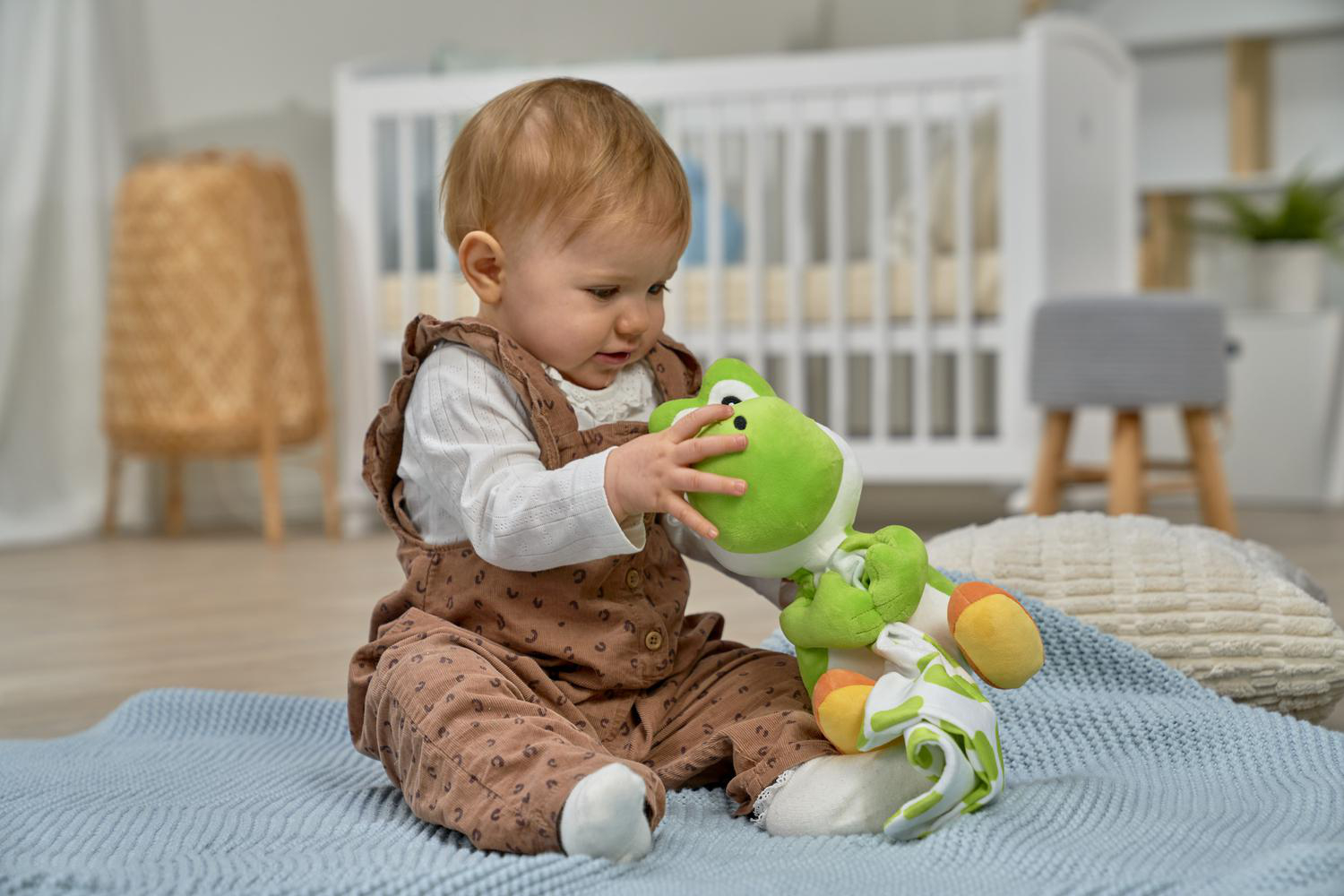 Ein Baby sitzt auf einer blauen Decke und spielt mit einem grünen Yoshi-Plüschtier.