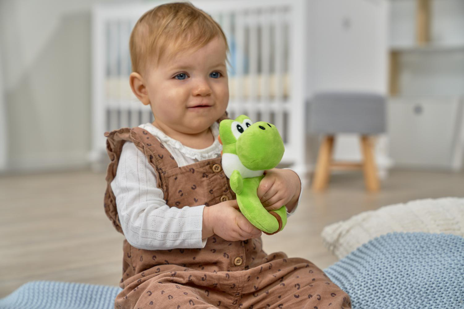 Ein Baby sitzt auf einer Decke und hält eine grüne Yoshi-Plüschfigur.