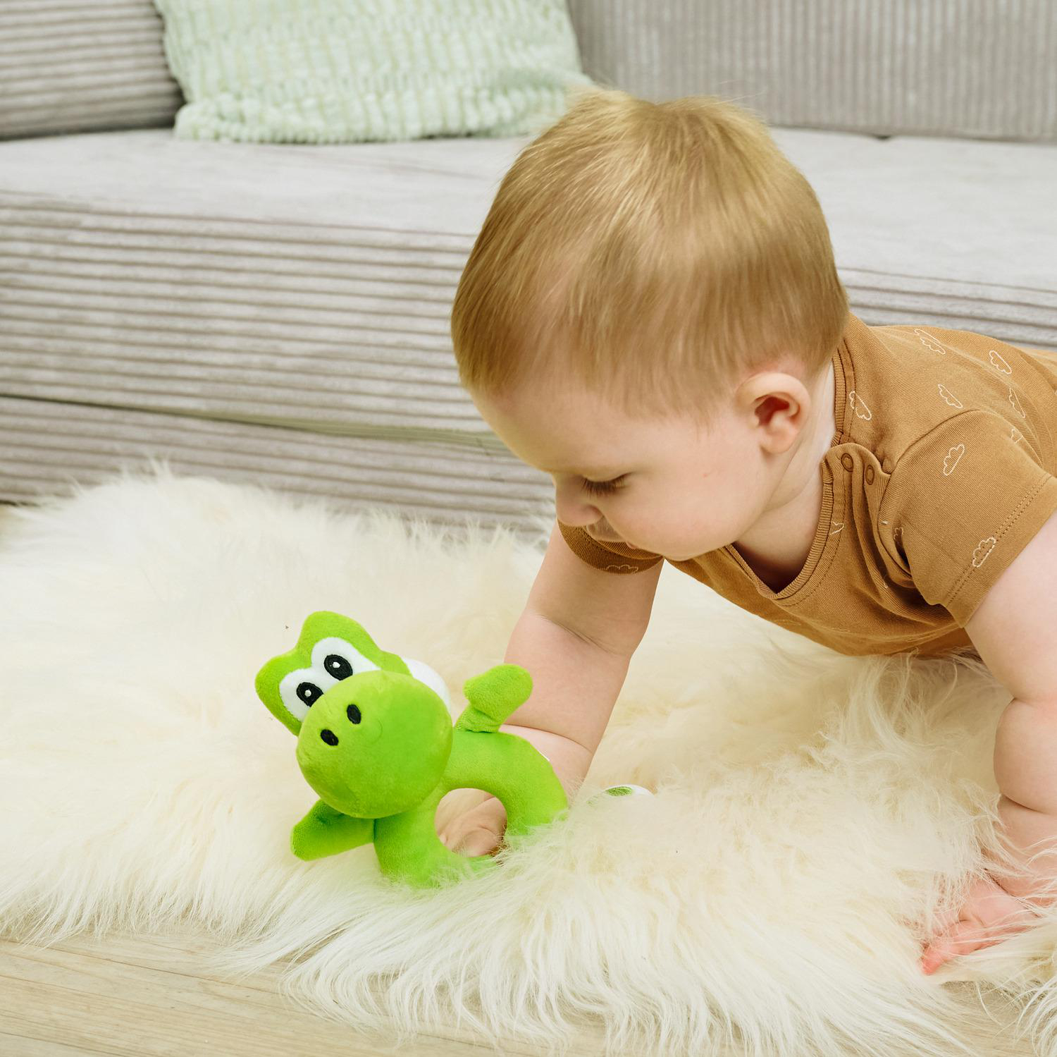 Baby krabbelt auf einem weißen Teppich und greift nach einem grünen Spielzeug.