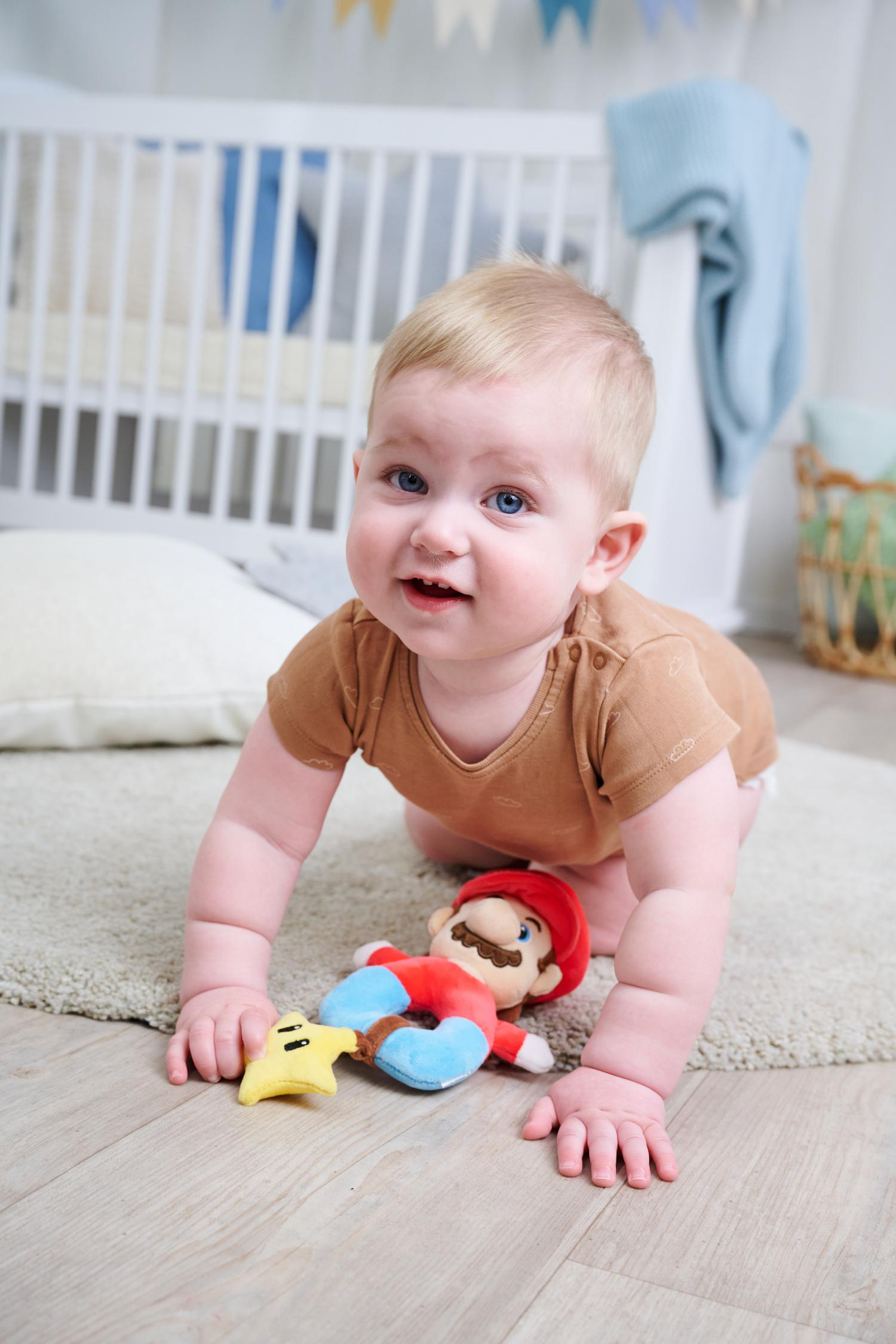 Ein Baby krabbelt auf einem Teppich neben einem Mario-Plüschtier und einem Sternenspielzeug.