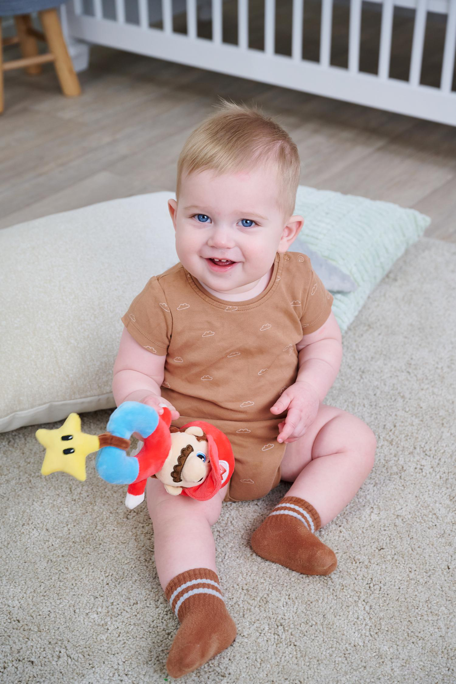 Ein lächelnder kleiner Junge mit blauen Augen sitzt auf einem Teppich und hält ein Spielzeug.