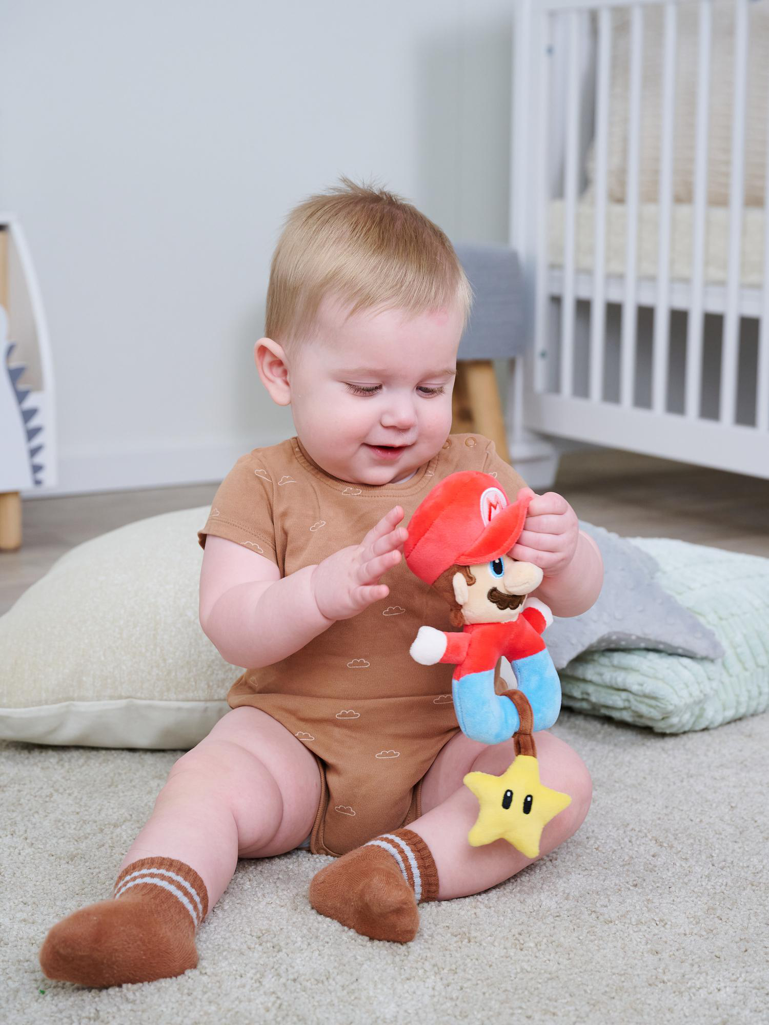 Ein Baby in brauner Kleidung spielt mit einer Mario-Puppe und einem Stern auf einem Teppich.