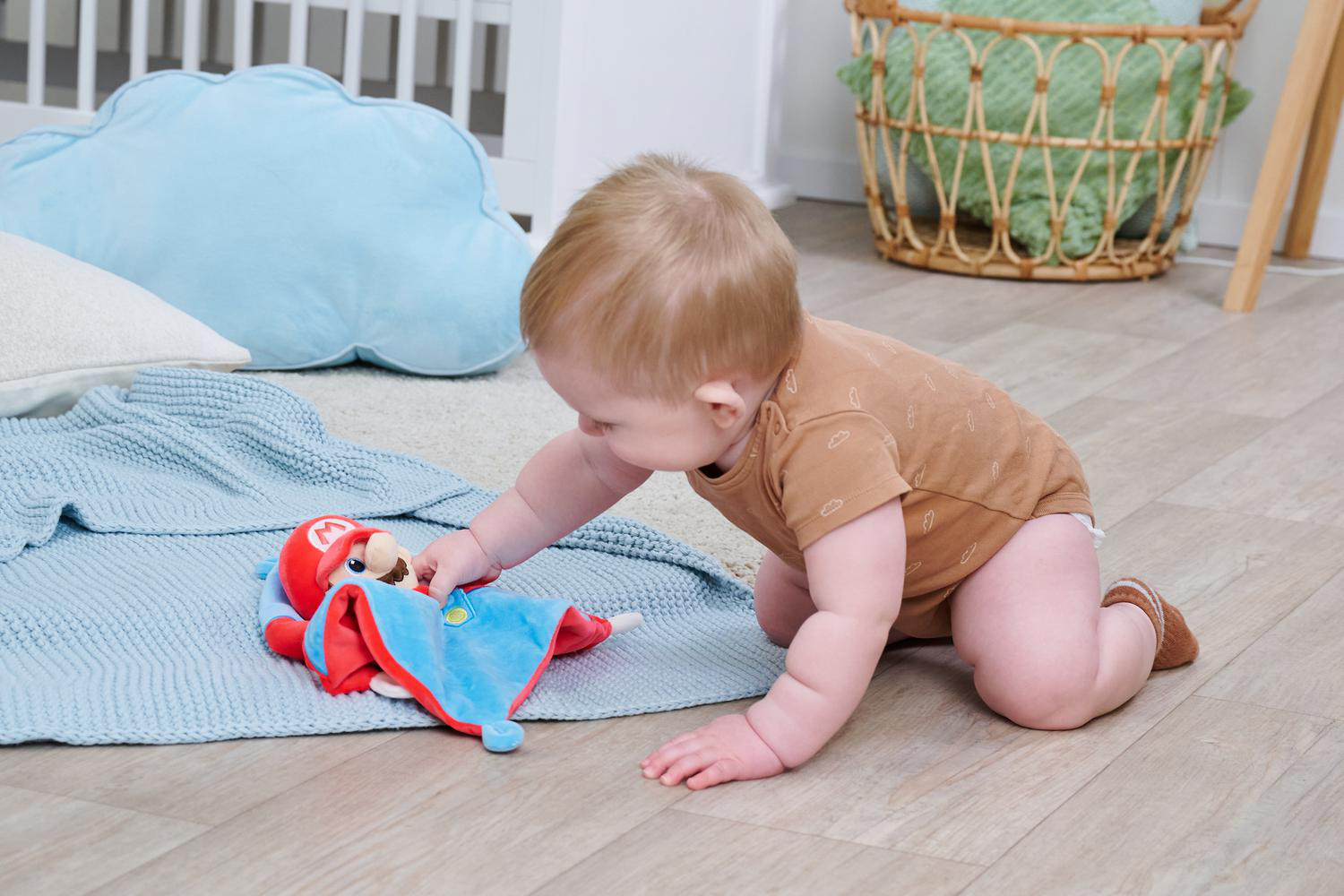 Baby krabbelt auf dem Boden und spielt mit einer Mario-Puppe auf einer Decke.
