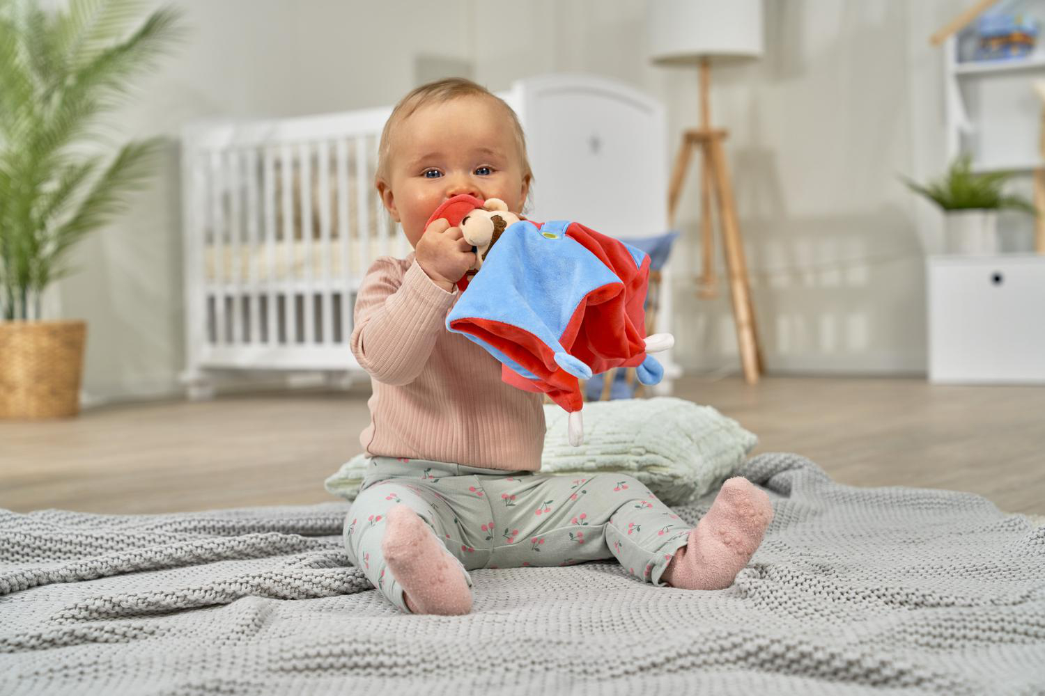 Ein Baby sitzt auf einer Decke und spielt mit einem bunten Spielzeug.