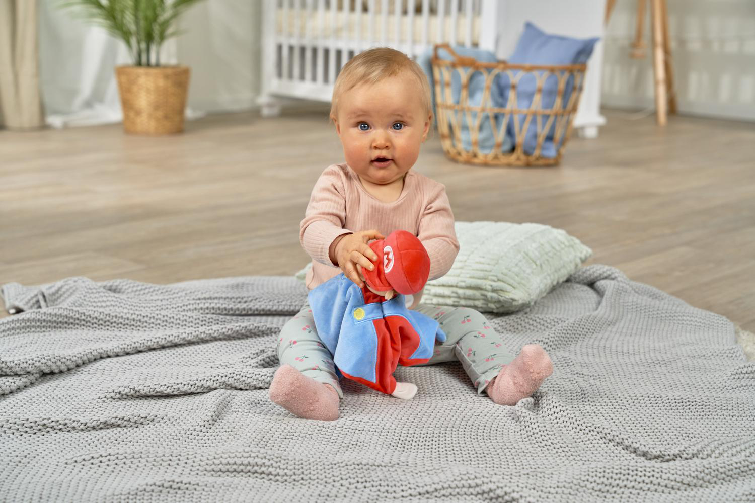 Ein Baby sitzt auf einer Decke und spielt mit einem roten und blauen Stofftier.