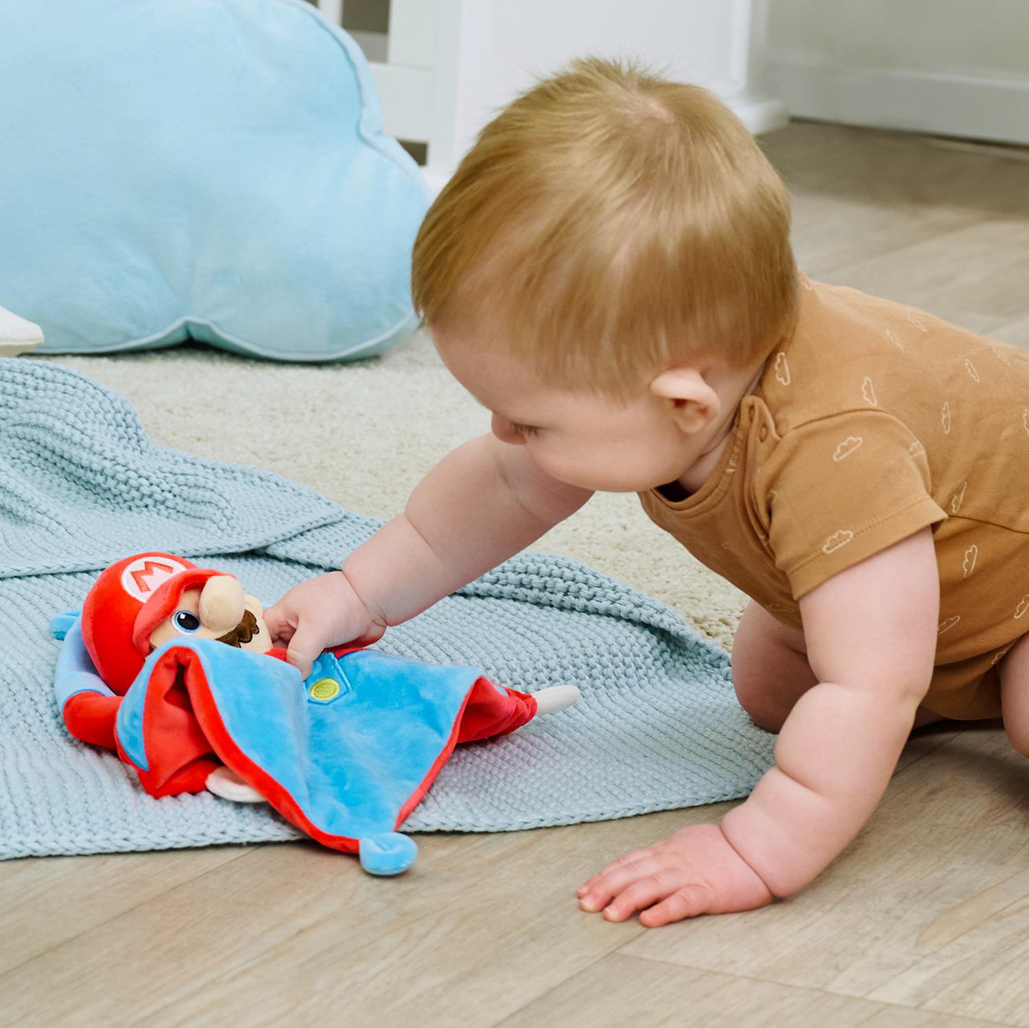 Ein Baby im braunen Strampler krabbelt auf ein Mario-Plüschtier auf einer blauen Decke zu.