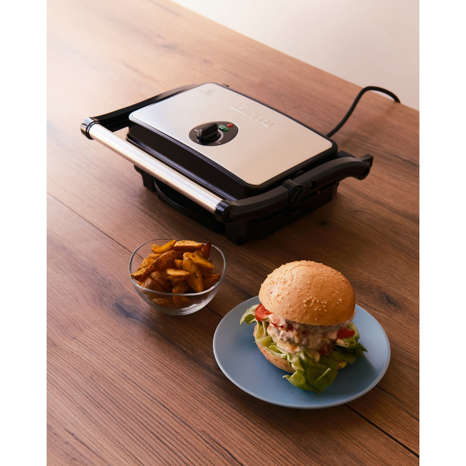 Una piastra per panini con hamburger e patatine su un tavolo di legno.