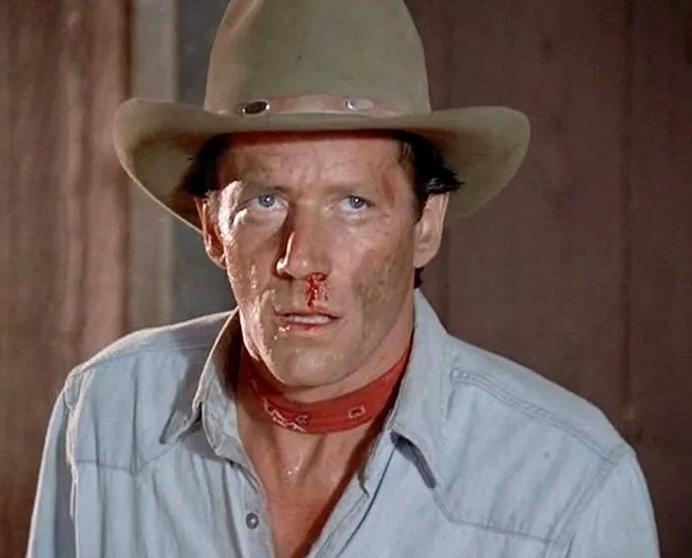 Ein Mann mit Cowboyhut, blauem Hemd und rotem Halstuch blutet aus der Nase.