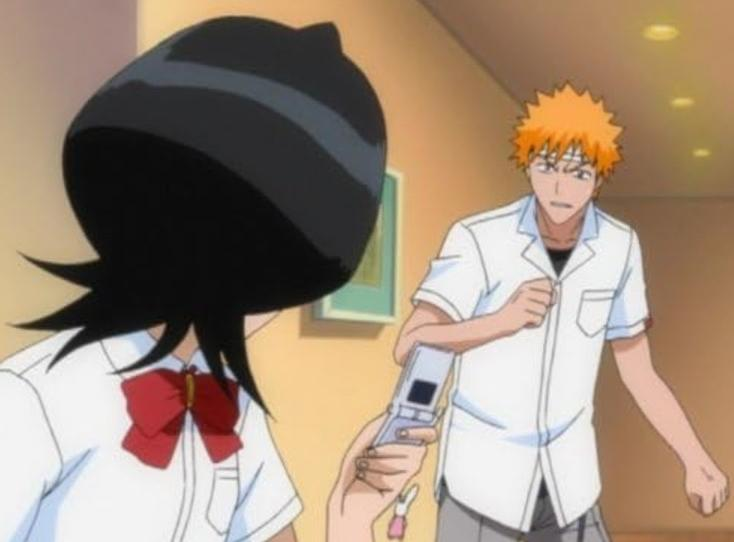 Ein Anime-Charakter mit orangefarbenem Haar hält ein Handy, während eine andere Figur mit schwarzem Haar daneben steht.