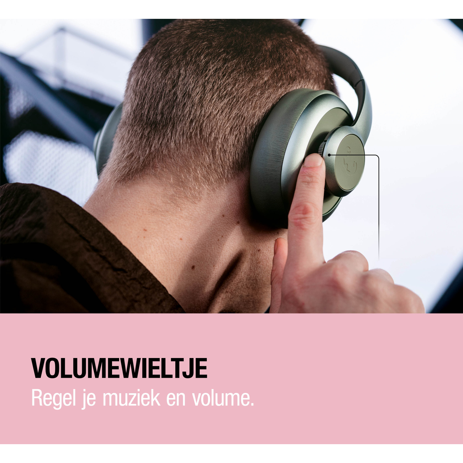 A man wearing headphones adjusts the volume dial with his finger.