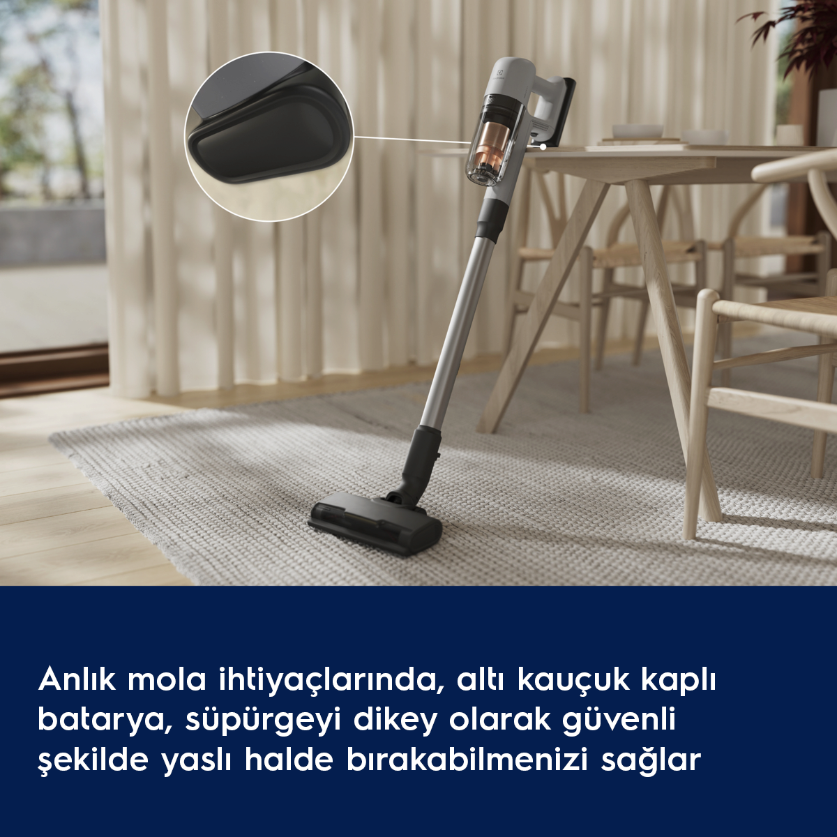 Gri kablosuz süpürge, ahşap masa yanında halının üzerinde duruyor.