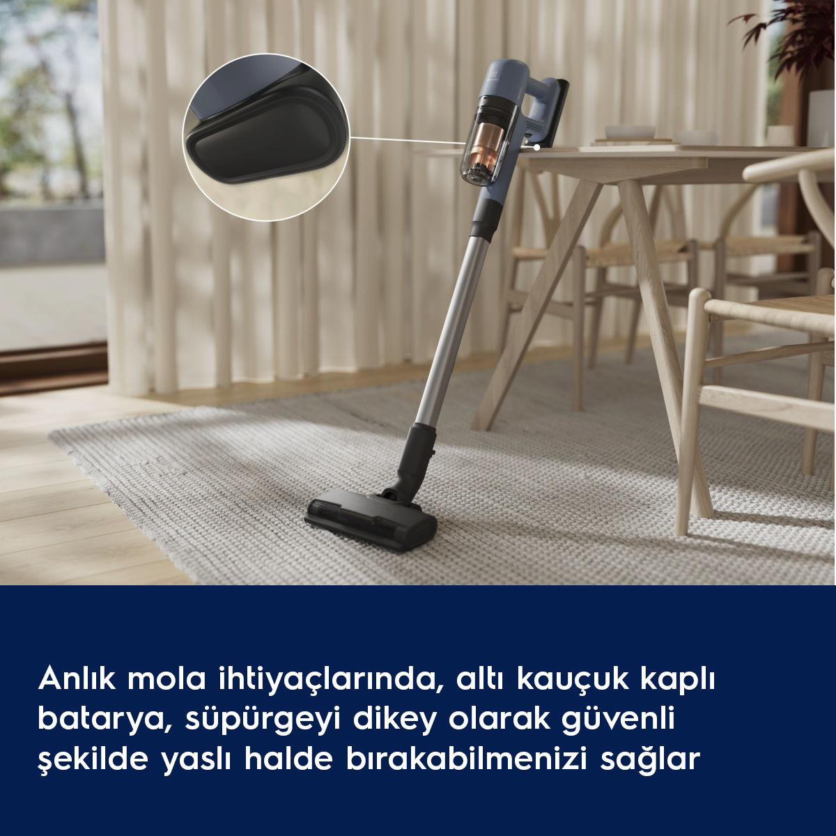 Mavi şarjlı süpürge, içeride bir halının üzerinde dikey duruyor.
