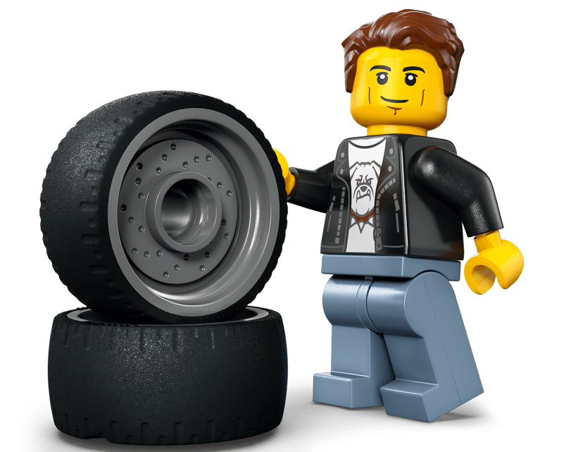 Ein Lego-Mann mit braunen Haaren und einem schwarzen Jackett steht neben zwei Autoreifen.