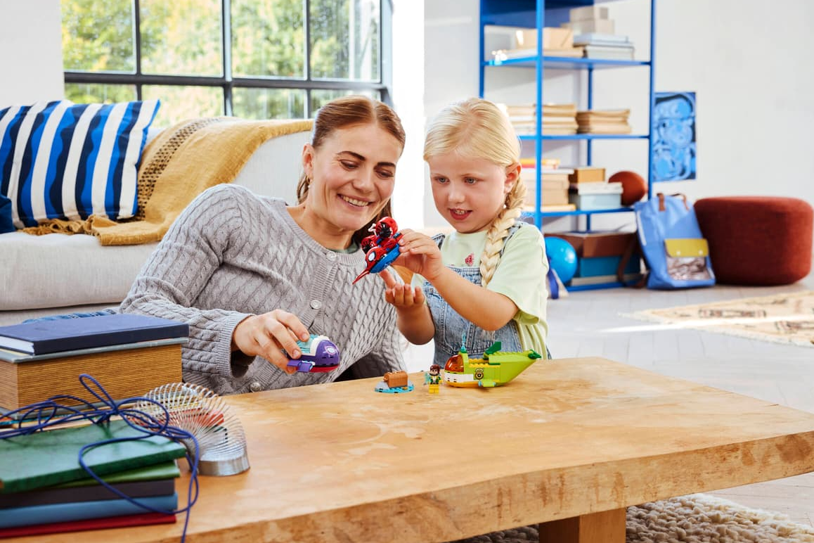 Eine Frau und ein Kind bauen LEGO auf einem Holztisch.