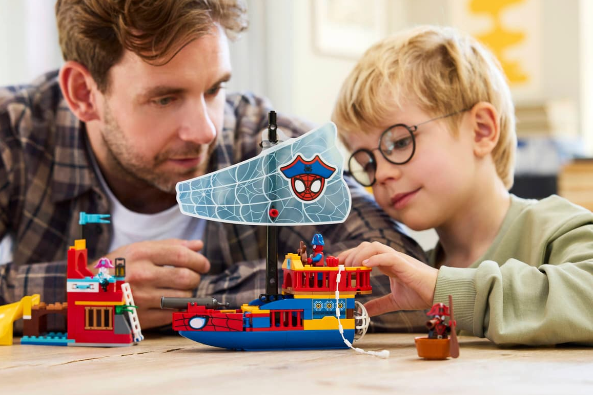 Vater und Sohn bauen ein Lego-Schiff mit Spiderman-Motiv.