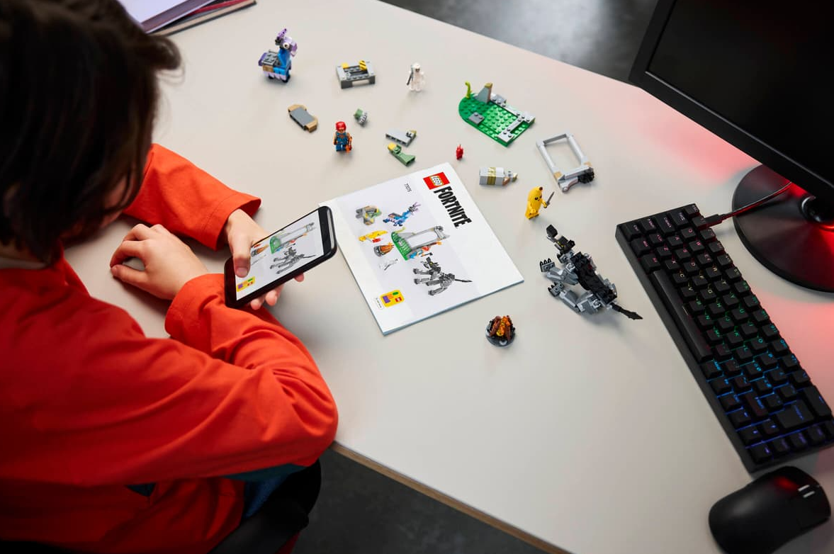 Kind baut Lego Fortnite auf einem Schreibtisch mit Handy, Tastatur und Maus.