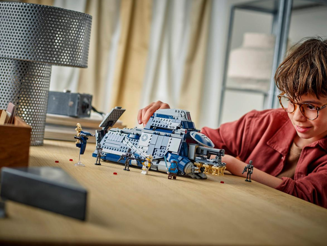 Ein Junge baut ein graublaues Raumschiff aus Lego-Steinen, mit Figuren auf dem Tisch.