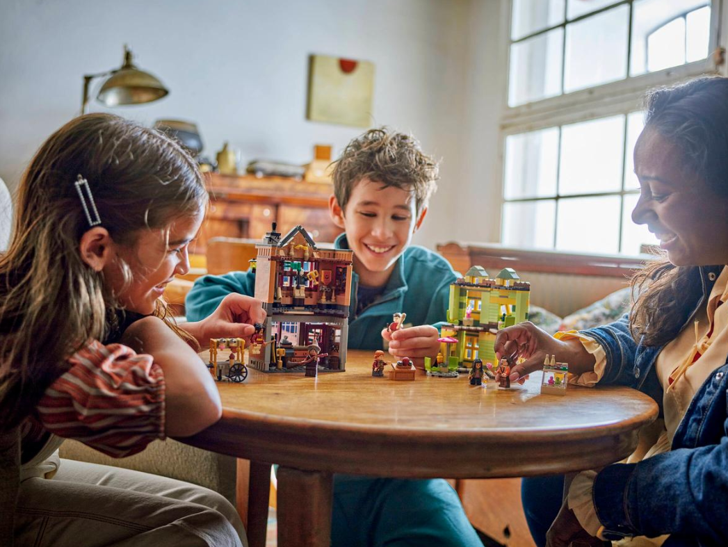 Drei Kinder spielen mit Lego-Häusern an einem Holztisch.