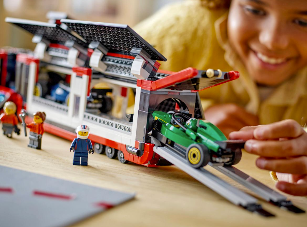 Kind spielt mit einem Lego-Transporter, der einen grünen Rennwagen lädt.