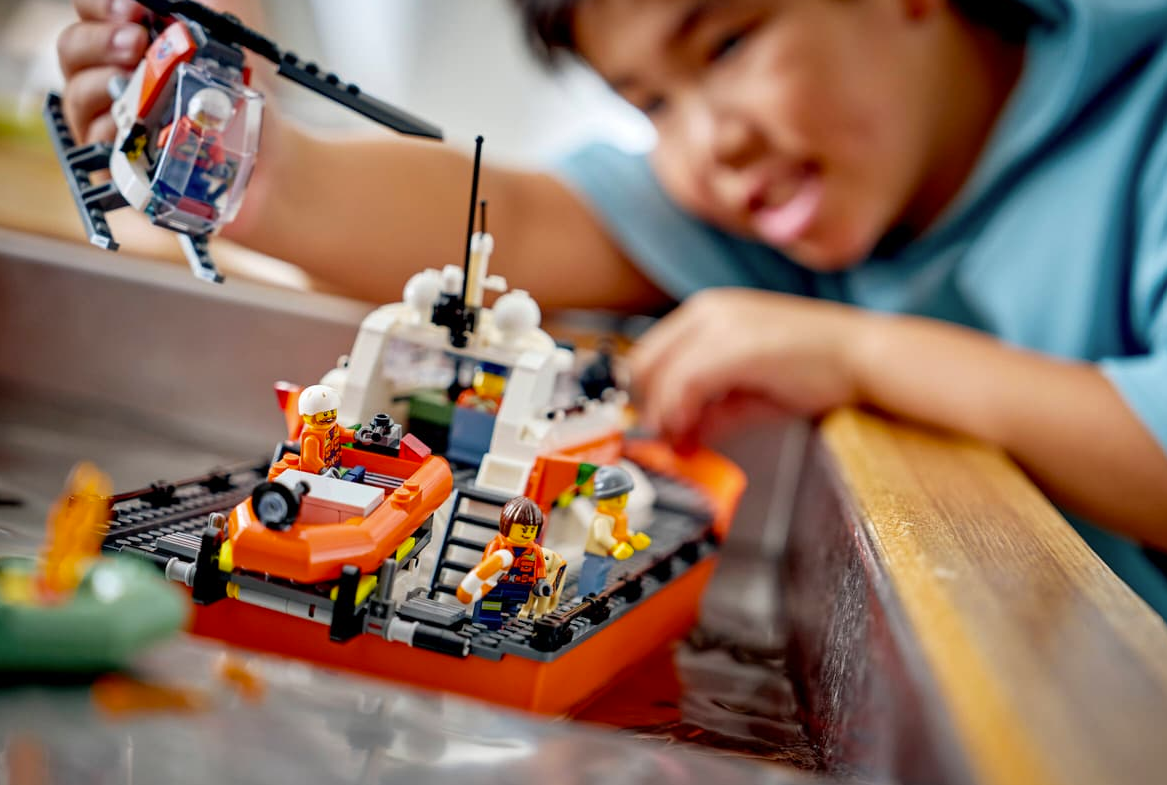 Ein Junge spielt mit Lego-Rettungsbooten und einem Hubschrauber im Wasser.