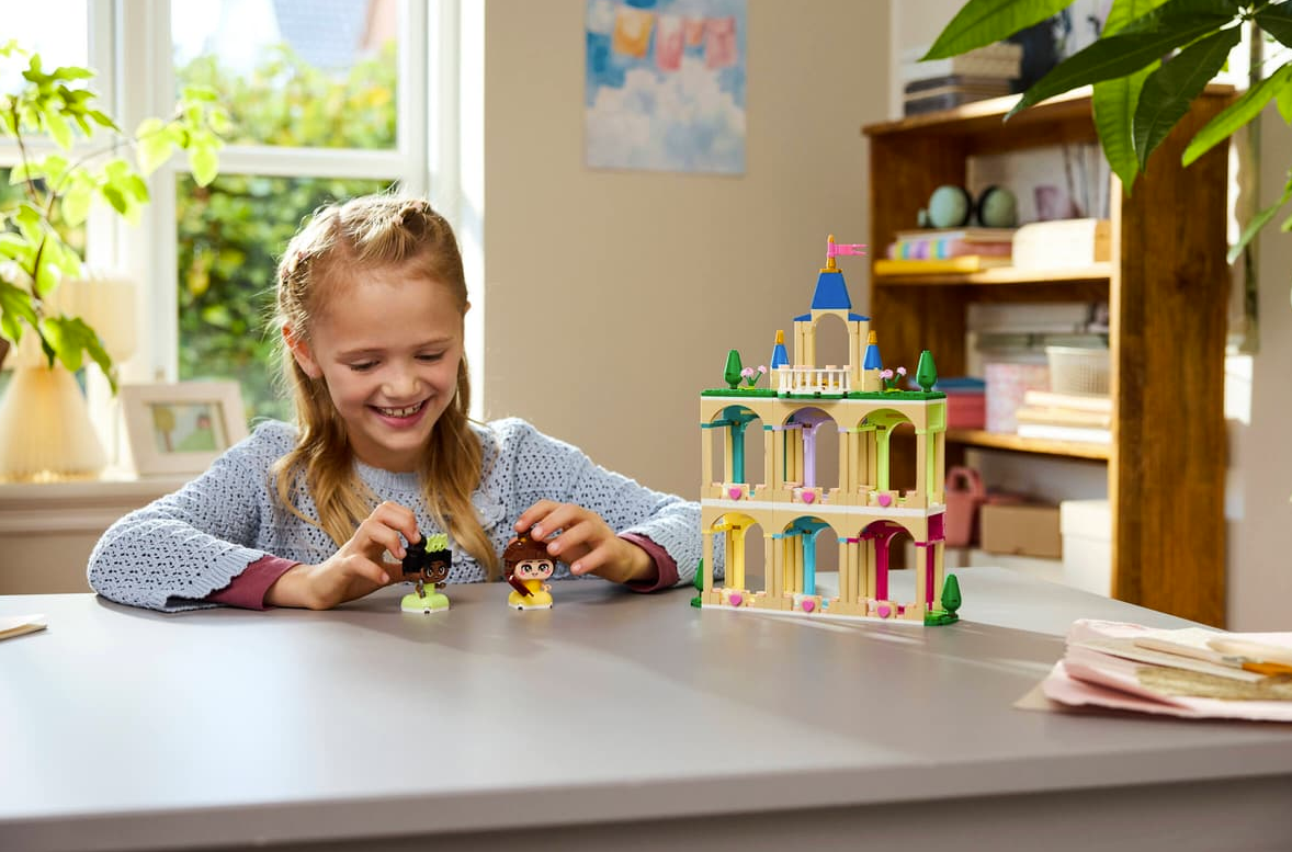 Ein Mädchen spielt mit Lego-Figuren und einem Lego-Schloss vor einem Fenster.
