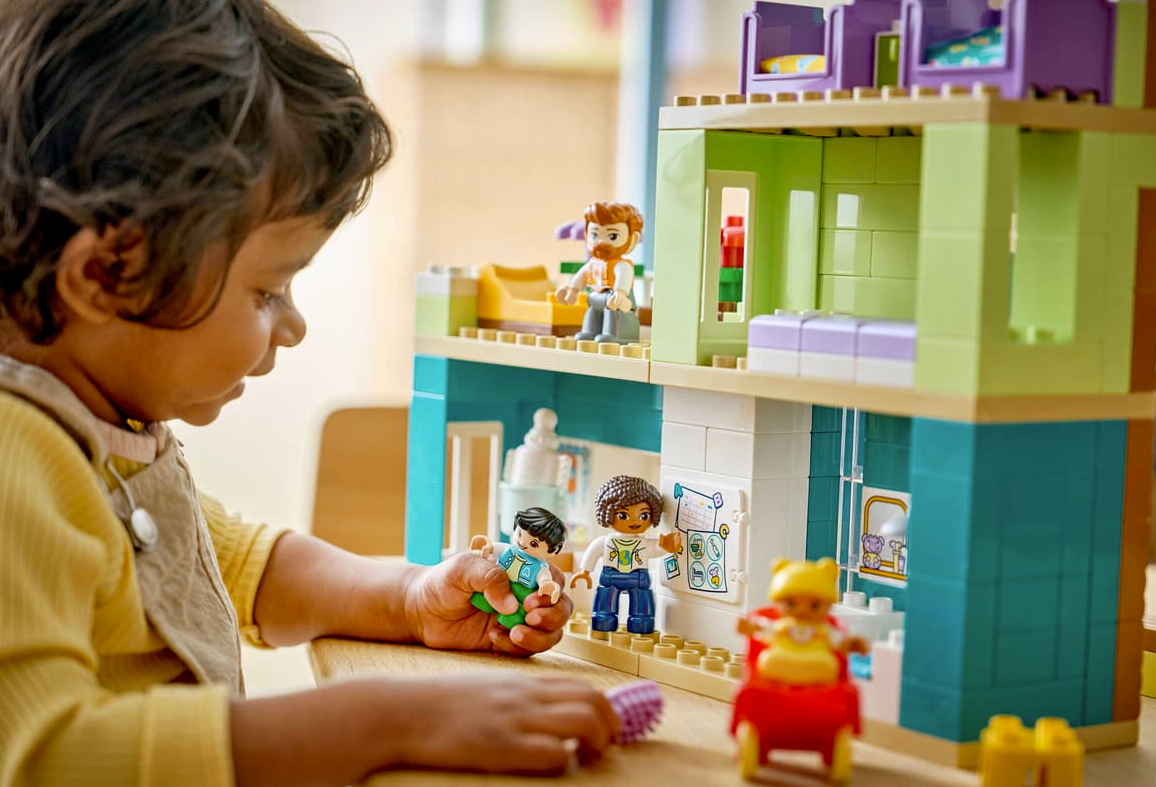Ein Kind spielt mit bunten Lego-Figuren und einem mehrstöckigen Haus.