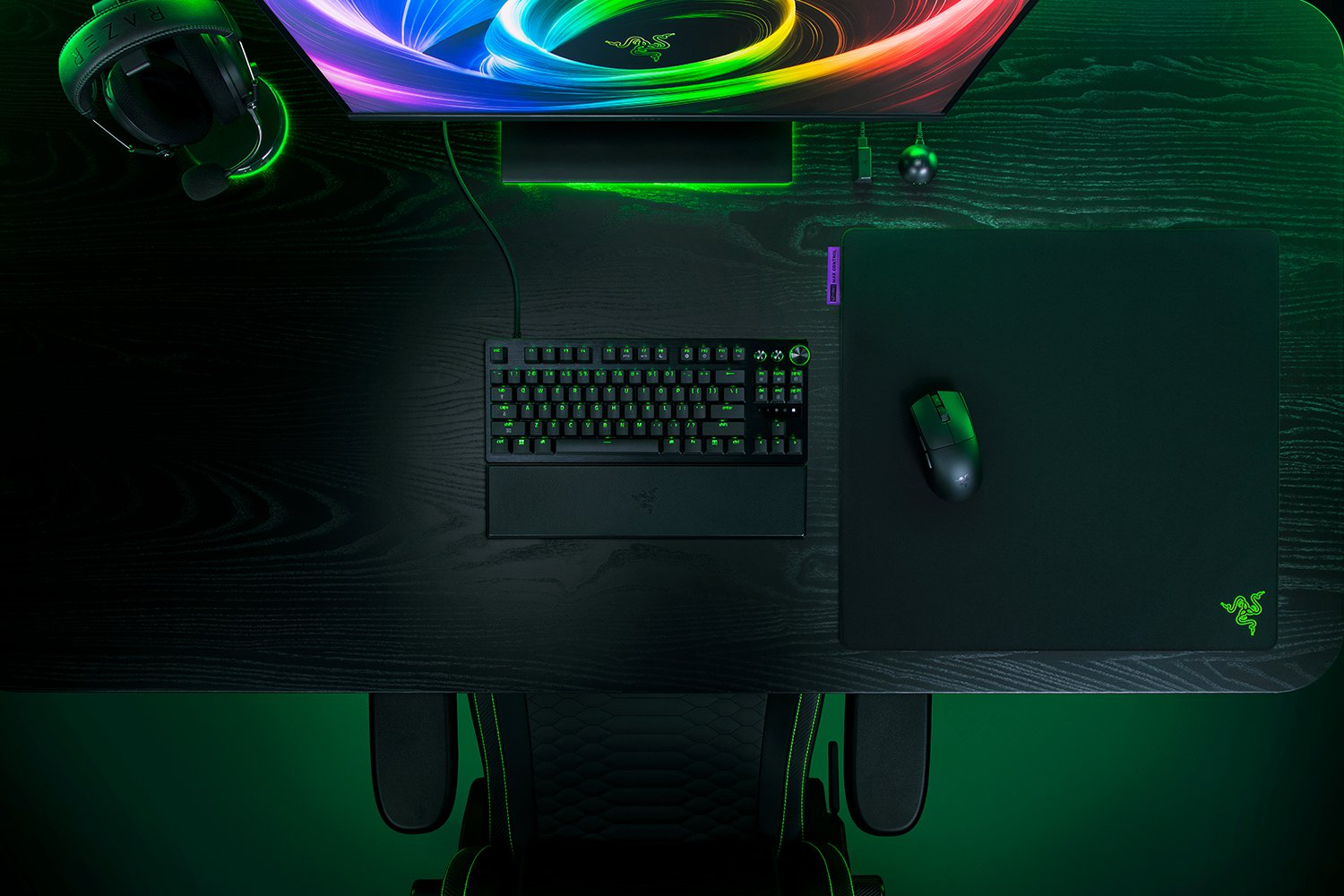 Un escritorio con equipo de juegos Razer, iluminado con luz verde.